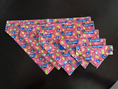 5 bandanas, one of each size, laying overlapped on a wooden surface.   Fabris is pawty time showing various party/dog related items printed on the fabric.