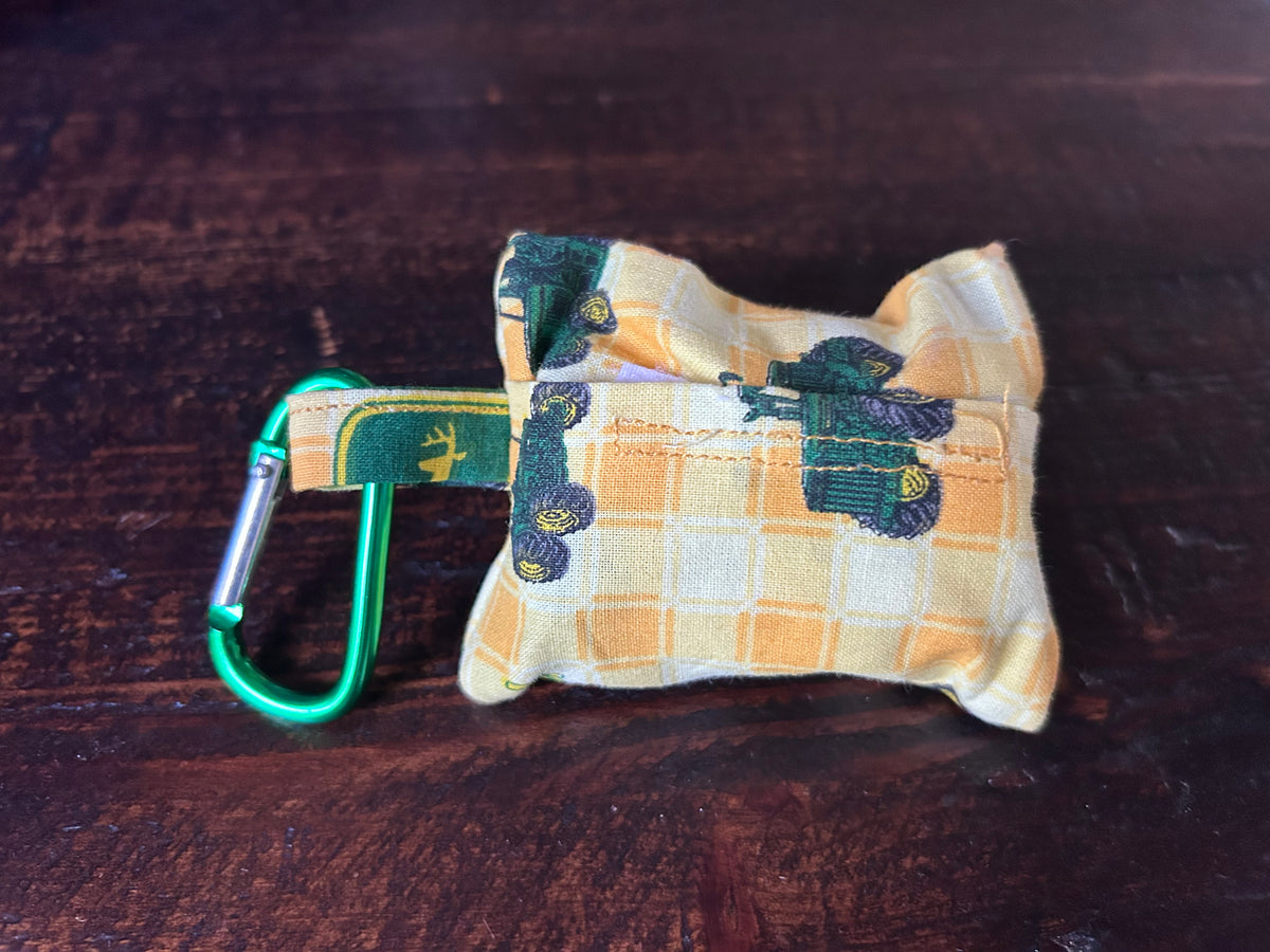 Waste Bag holder made of John Deer Fabric wth yellow checked background and green tractors lying on a wood surface.