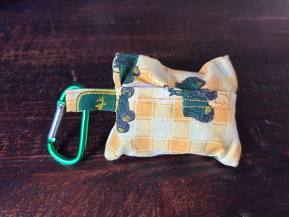 Waste Bag holder made of John Deer Fabric wth yellow checked background and green tractors lying on a wood surface.