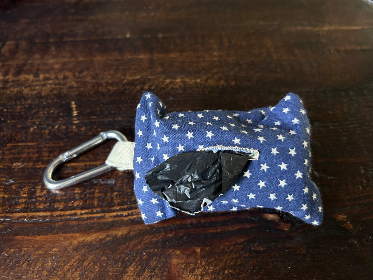 Waste Bag holder made of navy fabric with white stars containing a roll of black plastic bags  lying on a wood surface.