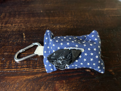 Waste Bag holder made of navy fabric with white stars containing a roll of black plastic bags  lying on a wood surface.